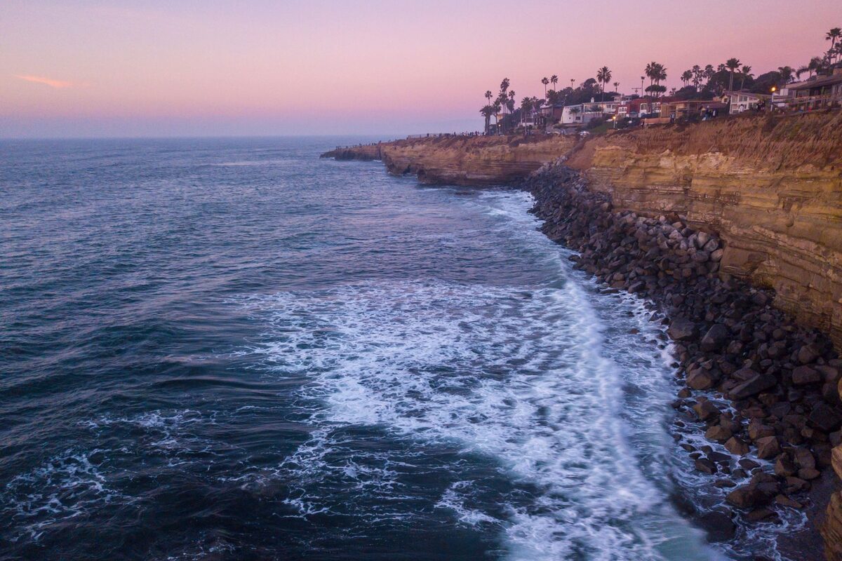 The San Diego coastline at dusk, with cliffs and palm trees above the water.