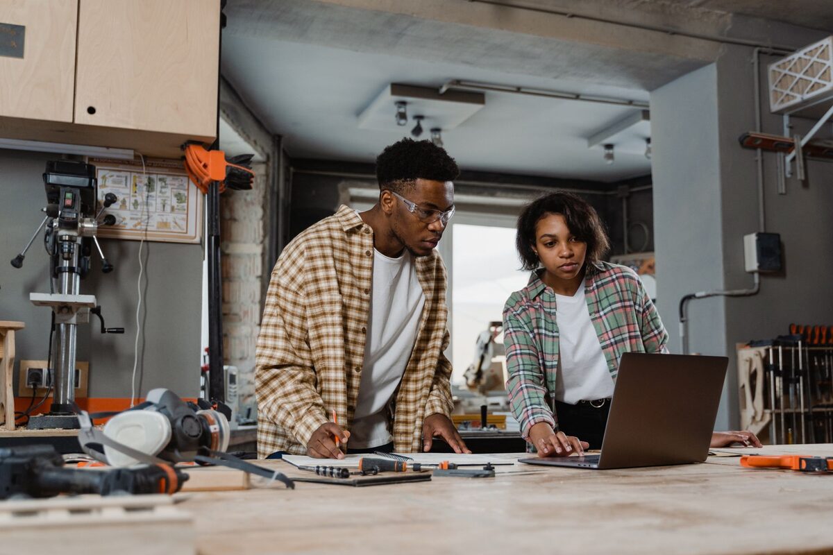 Two people reviewing work together at a bench in a small workshop.
